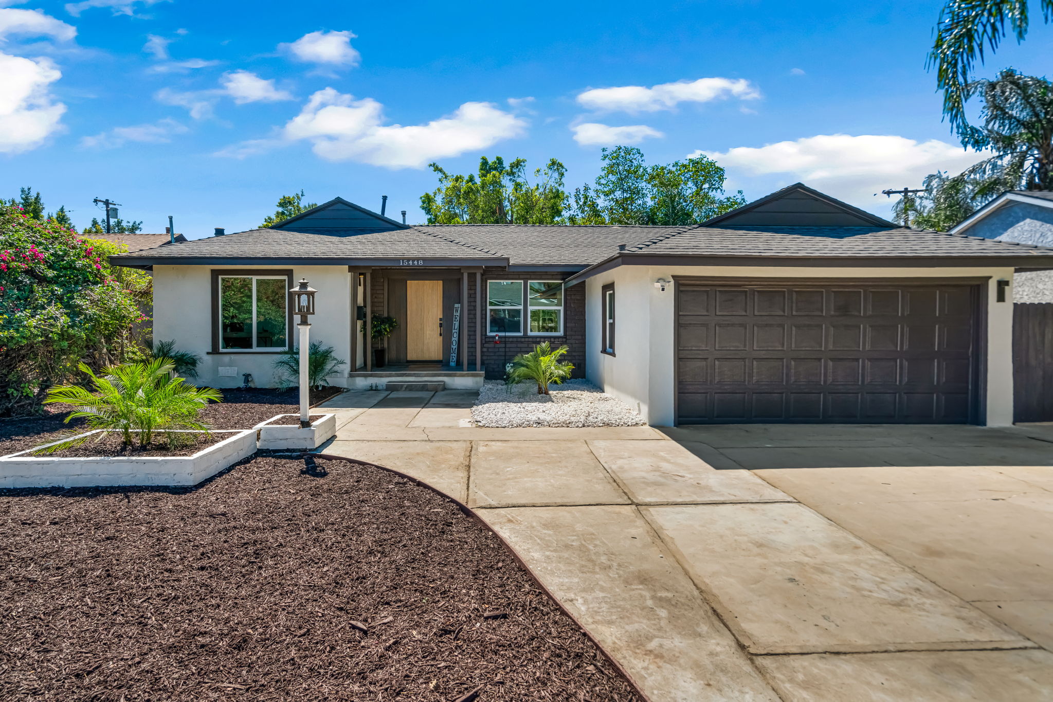 Front exterior — dark trim, 2-car garage, tropical landscaping